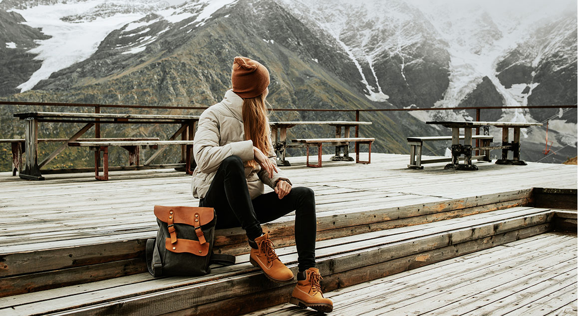 Viajante sentada em um deck de madeira apreciando a vista das montanhas